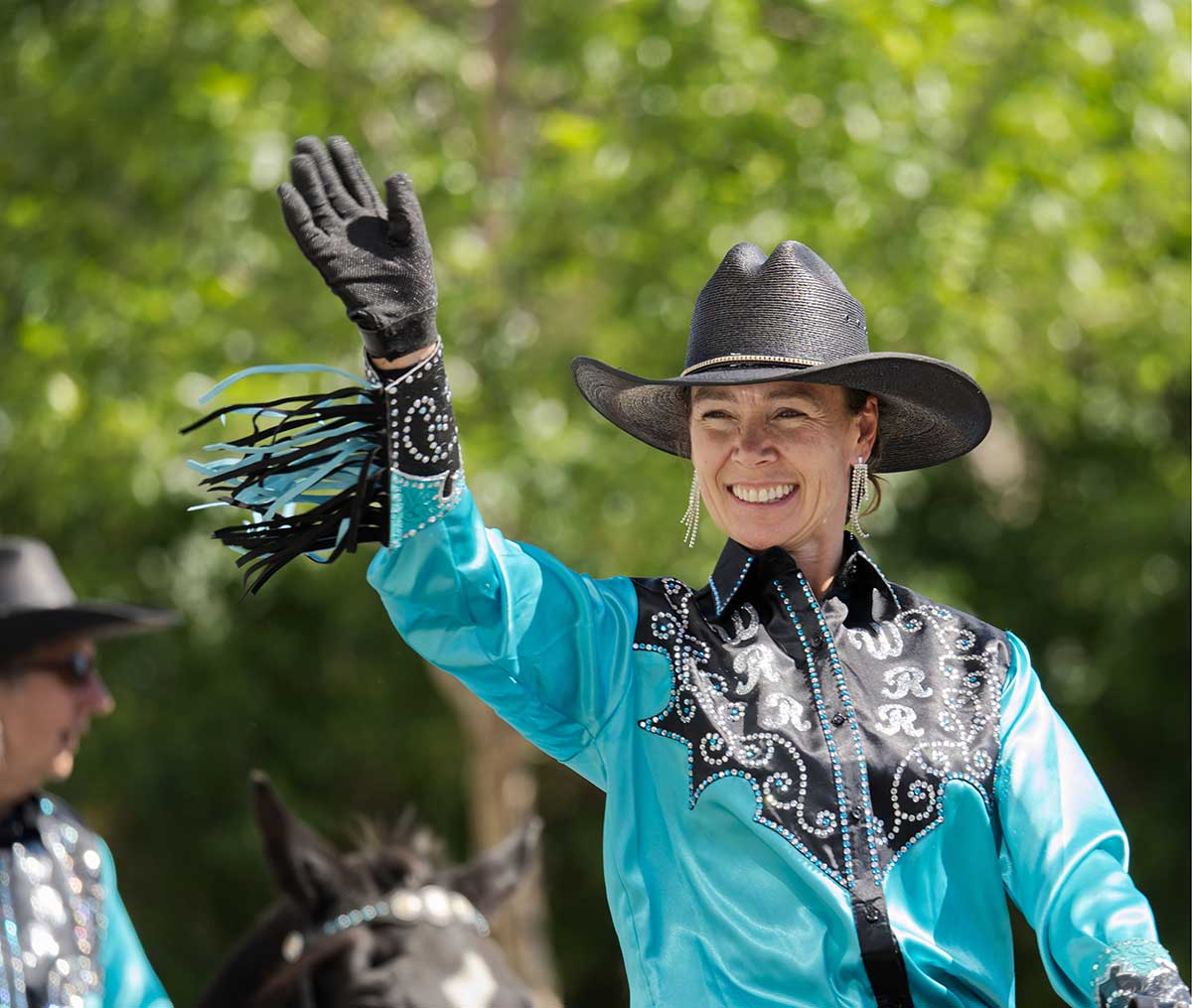 Fourth of July in Cody Wyoming: Your Complete 2026 Guide 3 Smiling cowgirl in turquoise Western outfit waving at the Cody Stampede Parade in Cody Wyoming