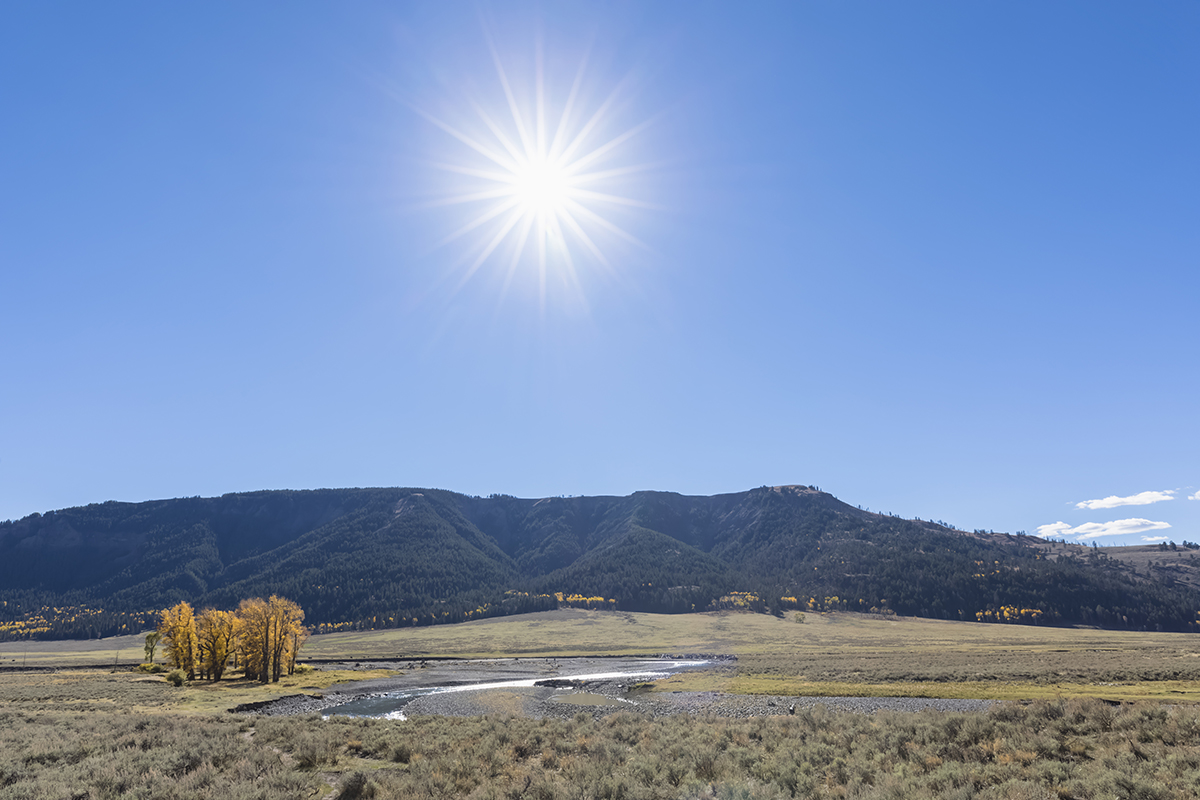 Yellowstone in July: What to Expect and How to Make the Most of It 5 Bright sun shining over Lamar Valley with mountains and a winding river in Yellowstone National Park