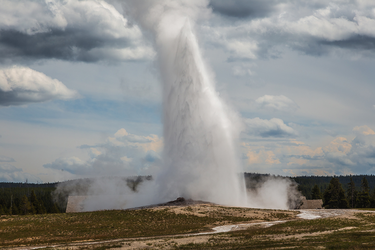 Yellowstone in July: What to Expect and How to Make the Most of It 9 Old Faithful geyser erupting with a tall plume of water and steam against a cloudy sky in Yellowstone National Park