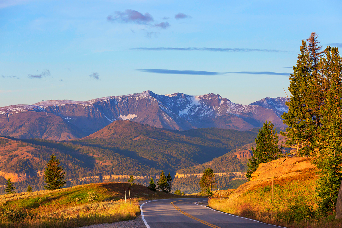 A winding road leading toward snow capped mountain peaks on the Chief Joseph Scenic Byway near Cody Wyoming