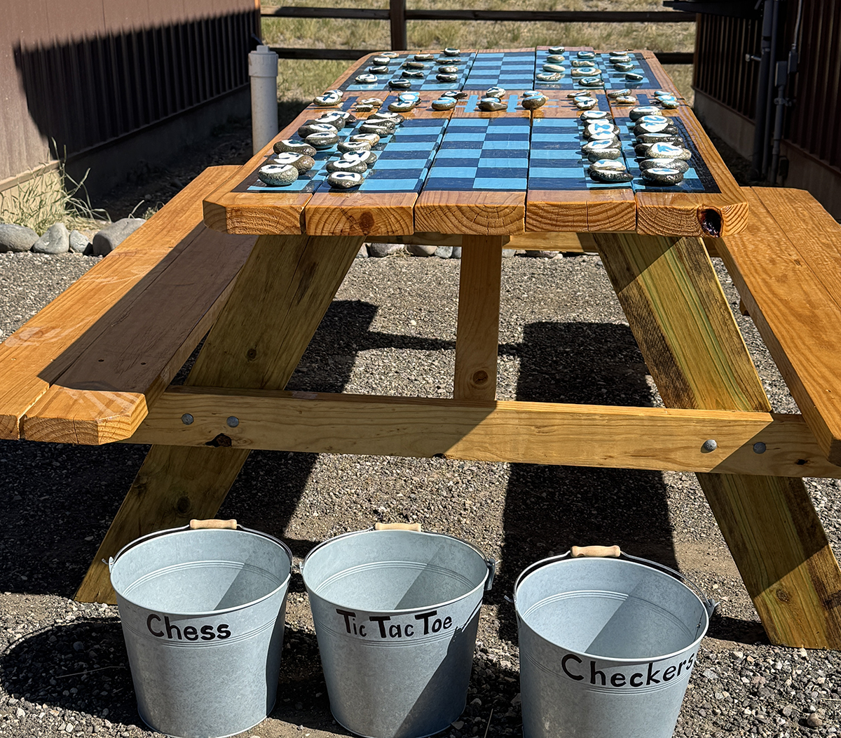 Yellowstone Group Camping: Why Old Faithful RV Park Is Perfect for Your Next Reunion or Rally 6 Outdoor picnic table with painted chess, tic tac toe, and checkers boards and labeled buckets of game pieces