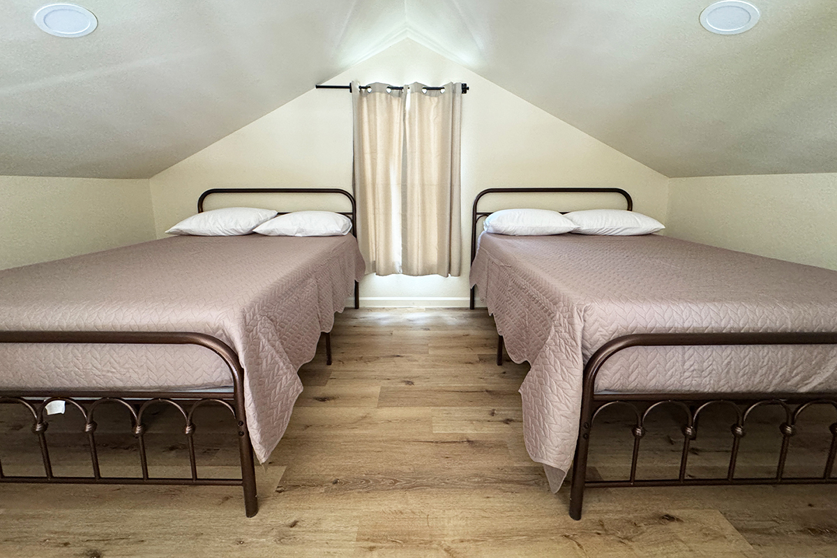 Loft bedroom with two full size beds under a sloped ceiling in a rustic cabin