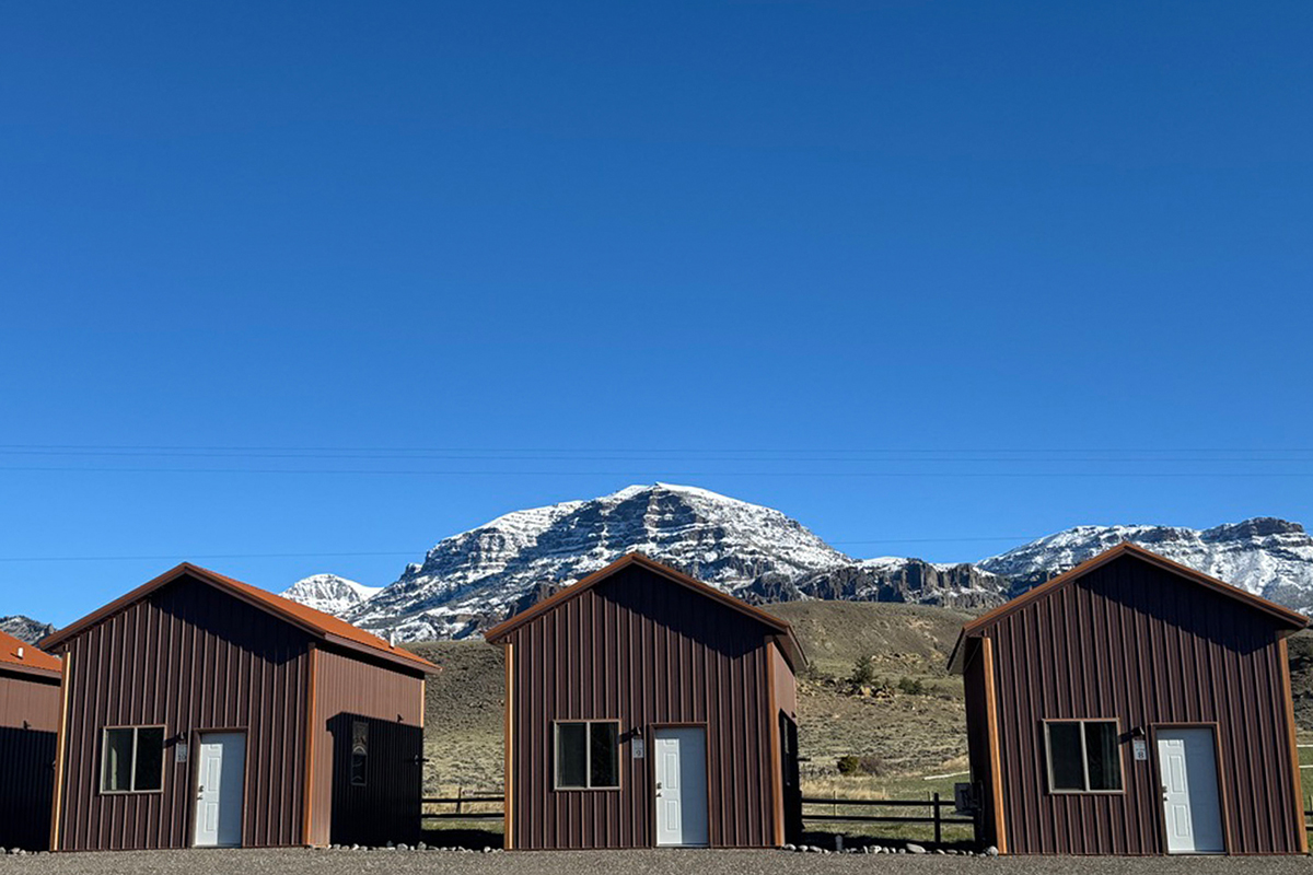 Three rustic cabins with snow capped mountains in the background at Old Faithful RV Park