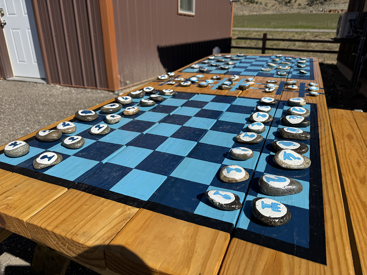 Thank You for an Amazing 2026 Season at Old Faithful RV Park 3 Painted rock chess and checkers pieces set up on a wooden picnic table at Old Faithful RV Park
