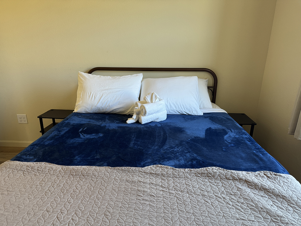 Cabin bed with a blue blanket and a rolled towel animal, a cozy place to rest on a longer stay near Yellowstone