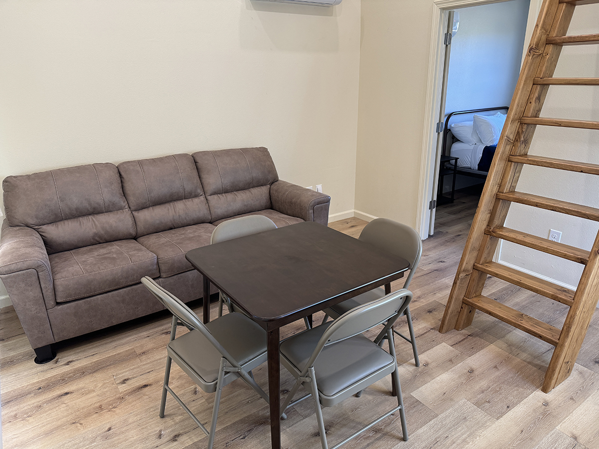 Cabin living room with a sofa, a table with four chairs, and a wooden loft ladder, one of our Cody Wyoming cabin rentals