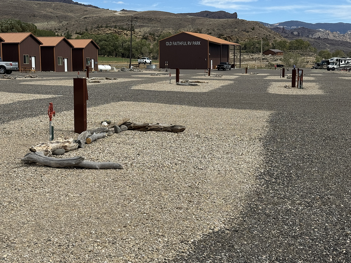 Full hookup RV sites with driftwood landscaping, rust colored cabins, and the Old Faithful RV Park building in Cody Wyoming