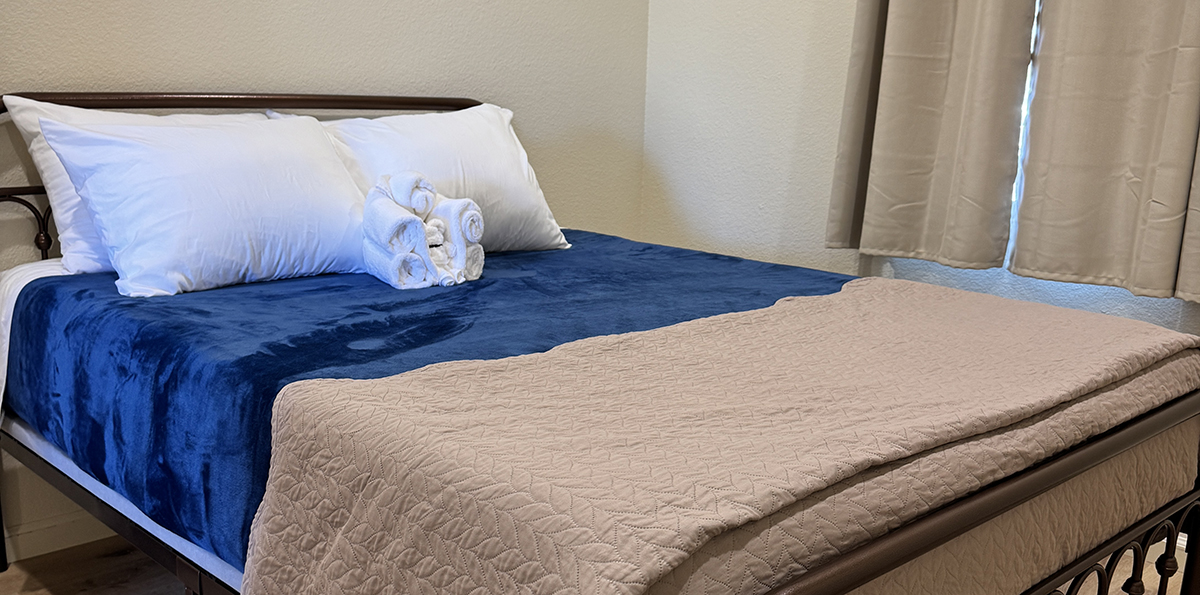 Camp Host Jobs Near Yellowstone: What Camp Hosting at Old Faithful RV Park Looks Like 8 Cabin bed made up with a blue blanket and rolled towels, a cleaning job for work camping near Yellowstone